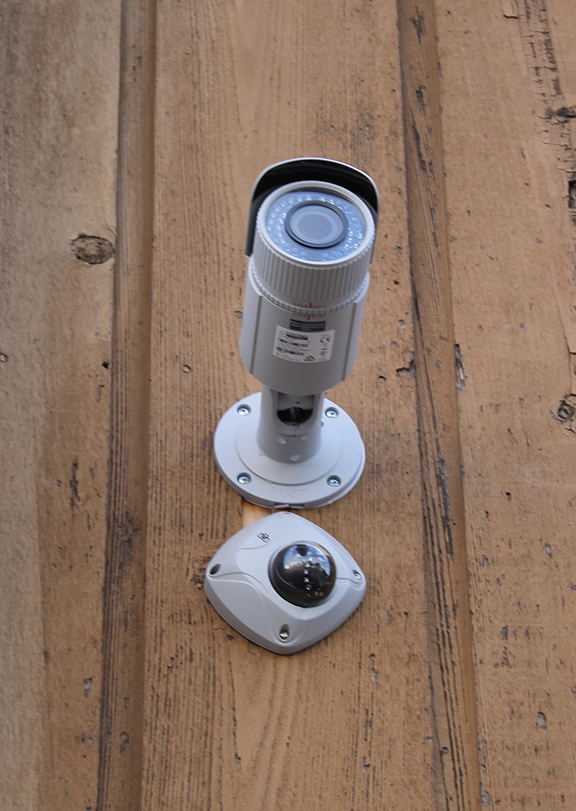 A WH Security surveillance camera mounted to a wooden wall. 